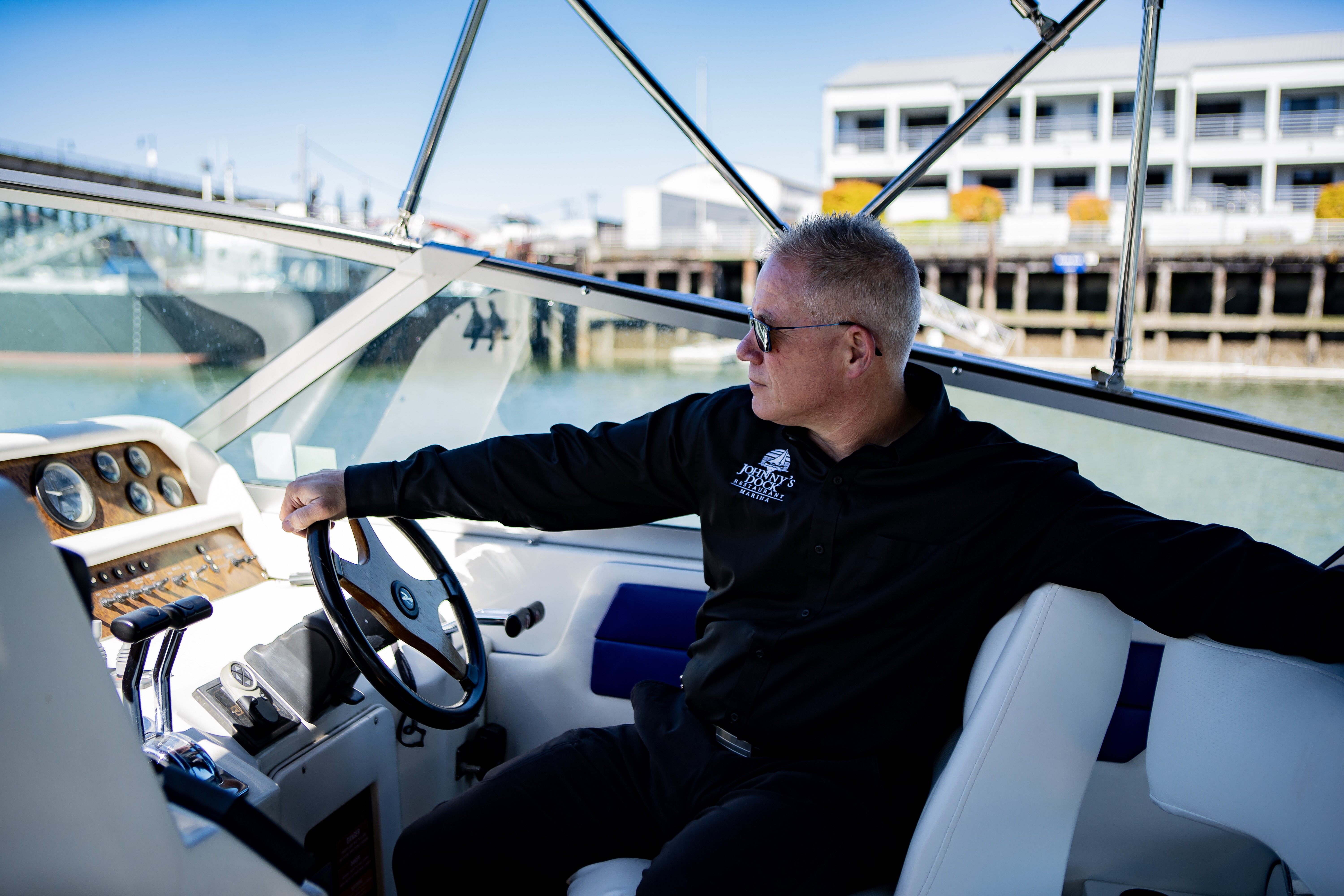 Steve Novotny at the helm of a motorboat at a sunny Pacific Northwest marina